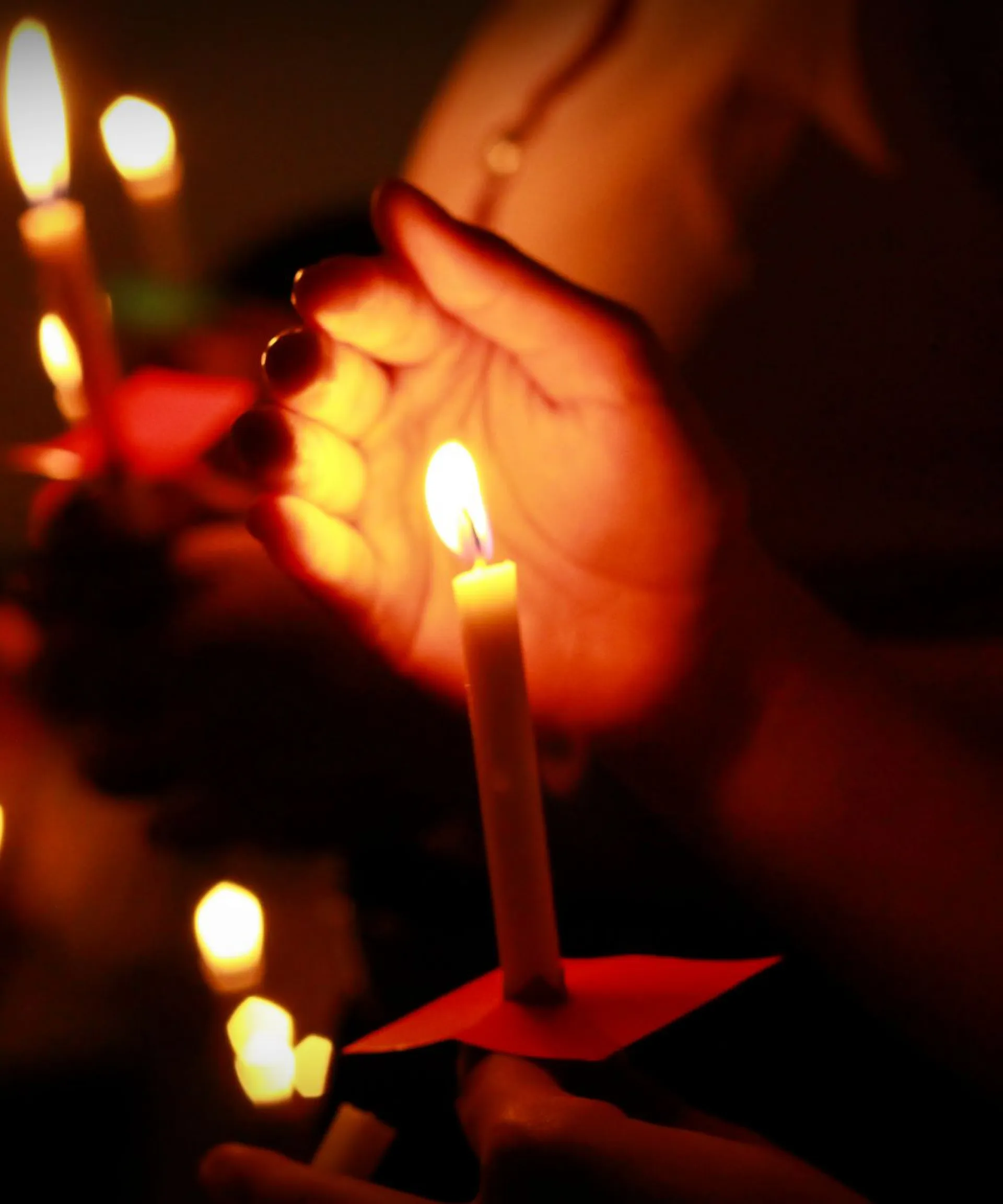 Hands holding lit candles in a dark setting.